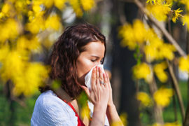 Woman Blowing Nose With Yellow Flowers Behind Her